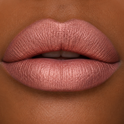 close-up lip image of darker skin model wearing Runway Rogue SilkGlam Long Wear Liquid Lipstick in Paparazzi, a frosted peachy nude shade